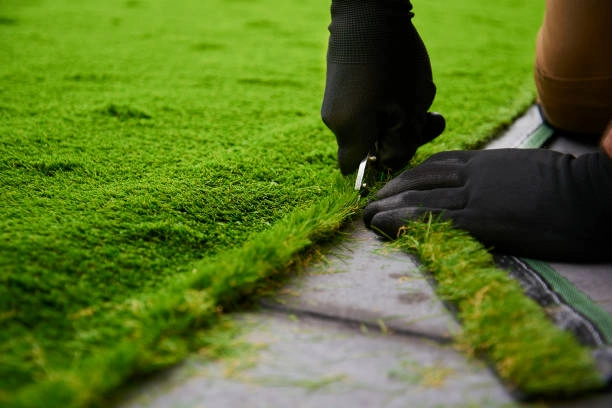 Gloved hands trimming artificial turf edges carefully for precise fit. -artificial lawn grass turf